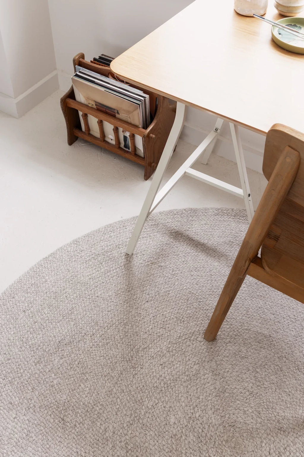 Grey round wool rug from Rugs for Good under a wooden chair and table set with a magazine holder on a light-colored floor.
