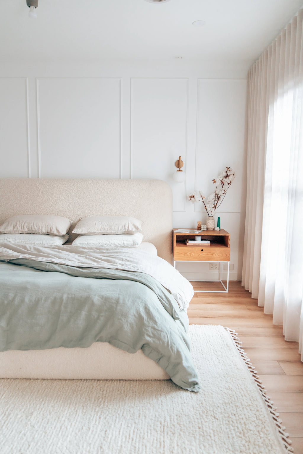 A bedroom setting with a bed and a nightstand, featuring a beige wool rug on the floor.