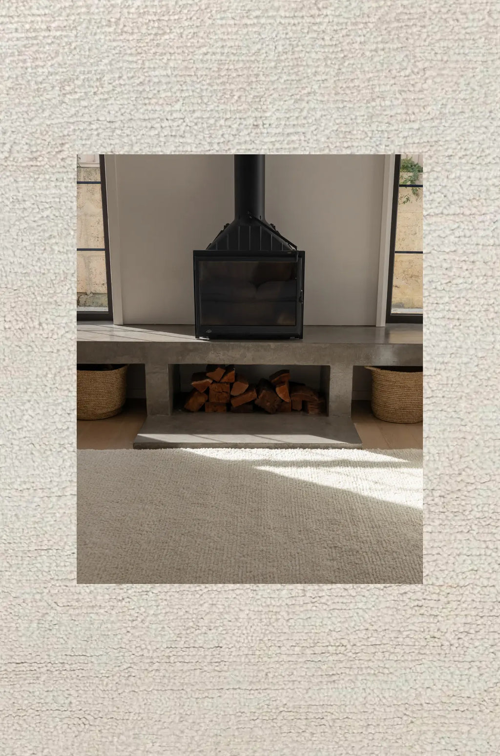 Rugs for good Sapna Ivory rug in a modern fireplace with a black metal stove and wooden logs in a neutral-colored room.
