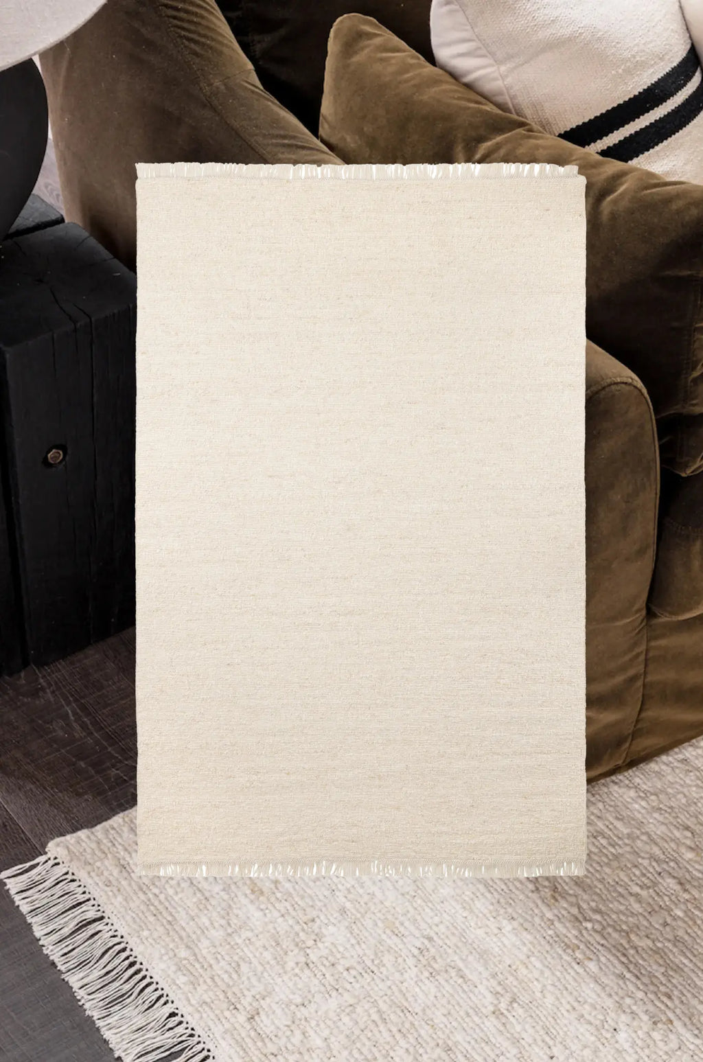 Beige rug with fringe on a floor with a Kiva in ivory rug next to a brown sofa.