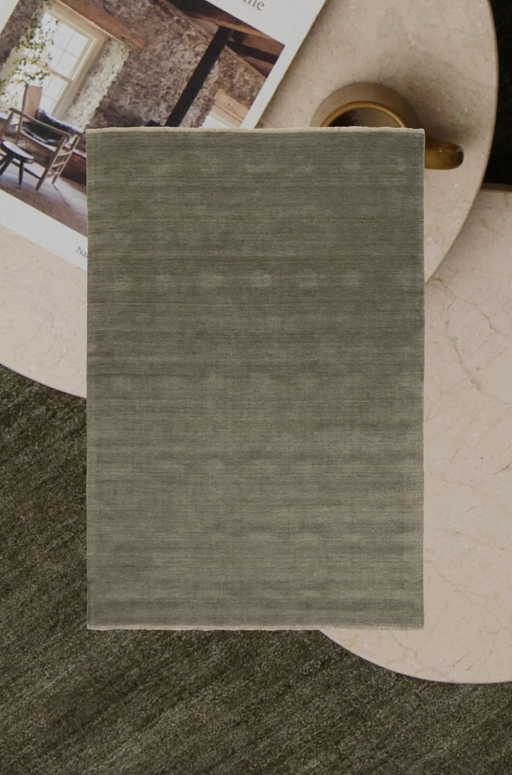 Green or Olive rug on a textured floor with a magazine and a vase in the background